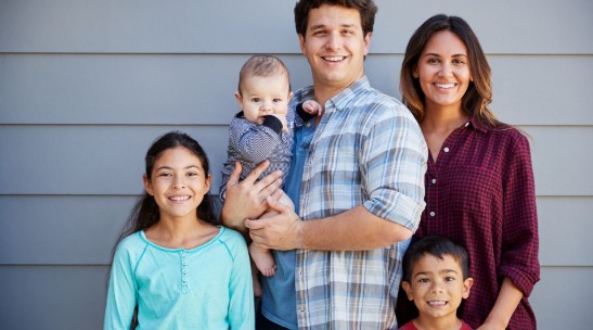 A family of 5 standing in front of a house.